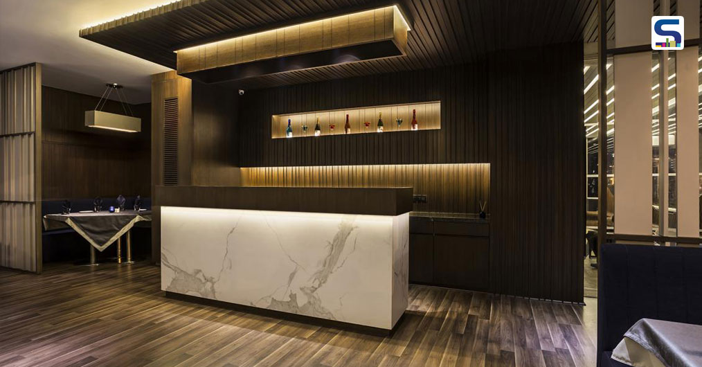 Door that leads to the kitchen service area is flushed with glass paneling. A cluster of four seating is meticulously conceived with wooden ceiling and flooring. Extensive use of wood can be seen in the flooring. Dual color tones with minimalistic fittings set in a bathroom of modern times